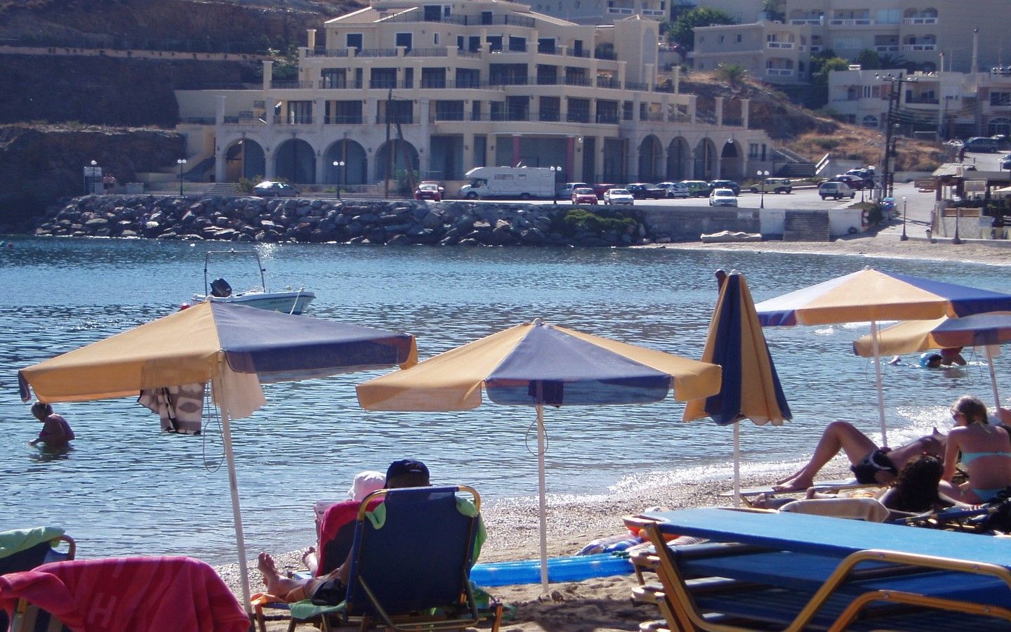 Una playa con sombrillas, sillas de descanso y un edificio al fondo.