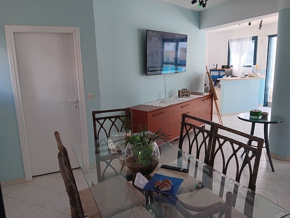 A dining area with a glass table, chairs, a potted plant, and a television mounted on the wall.