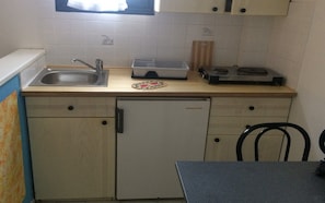 A compact kitchen with a sink, a small refrigerator, a toaster, and a wooden cutting board.