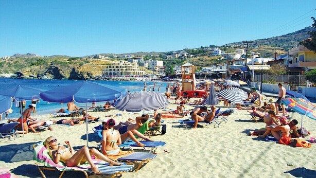 A beach with people sunbathing, umbrellas, and a lifeguard tower.