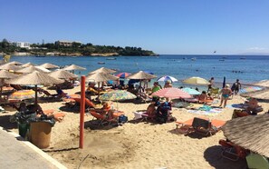 A beach with sun umbrellas, lounge chairs, and people relaxing. - Renia Hotel (Malevizi)