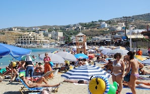 Una playa con gente tomando el sol, sombrillas y una torre de salvavidas.
