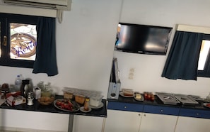 A kitchenette with a TV, a window with curtains, and various food items on the counter.