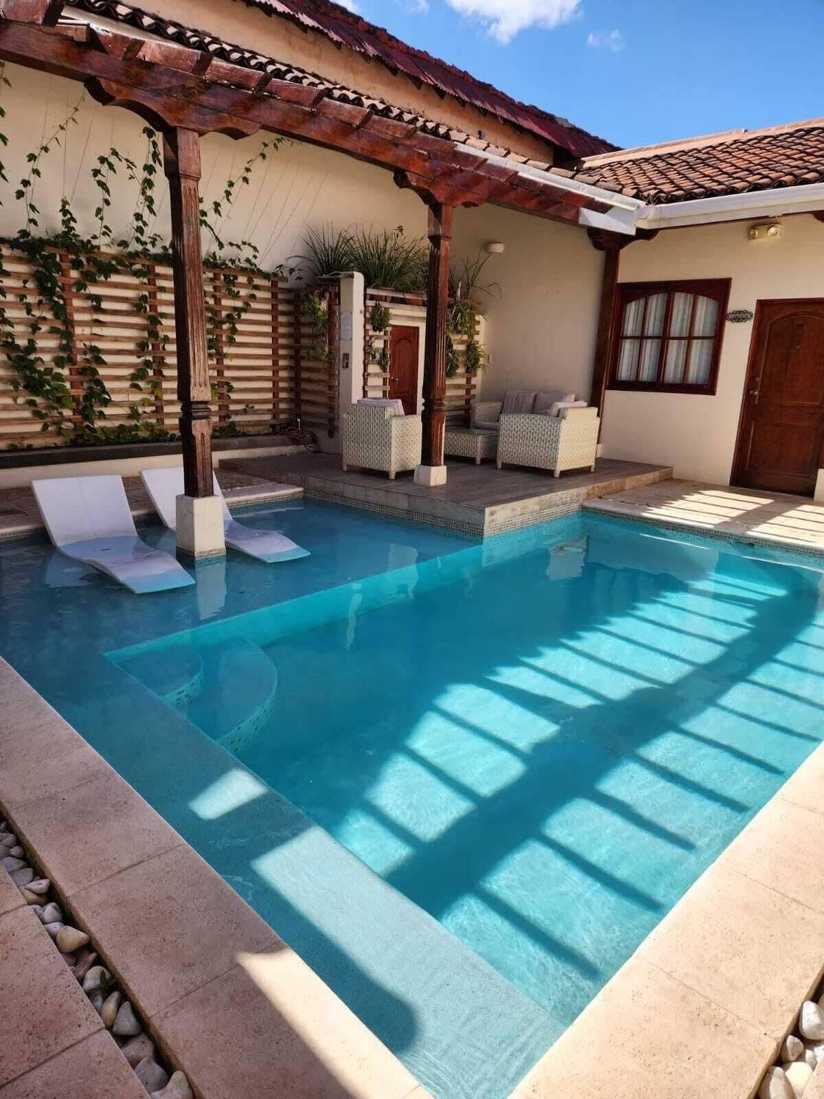 A swimming pool with a pergola, lounge chairs, and a covered seating area.