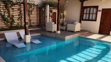 A swimming pool with a pergola, lounge chairs, and a covered seating area.