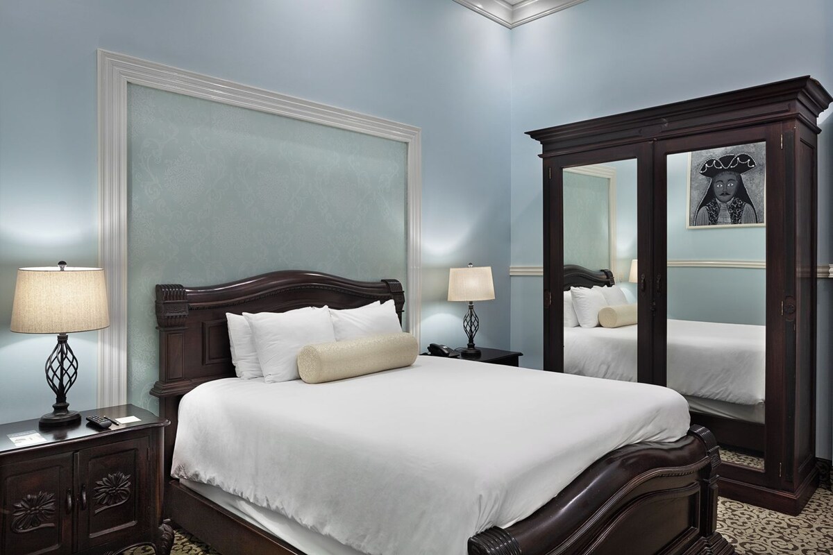 A neatly made bed with white linens, a dark wooden headboard, and two bedside lamps.