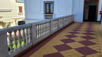 A balcony with a checkered floor, white walls, and a tiled roof.
