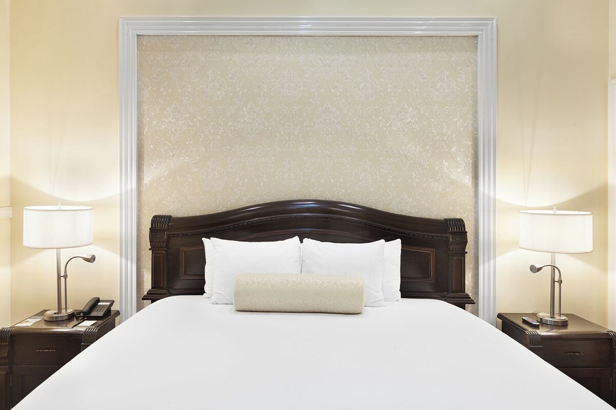 A hotel room with a large bed, two bedside tables, a telephone, and two lamps.