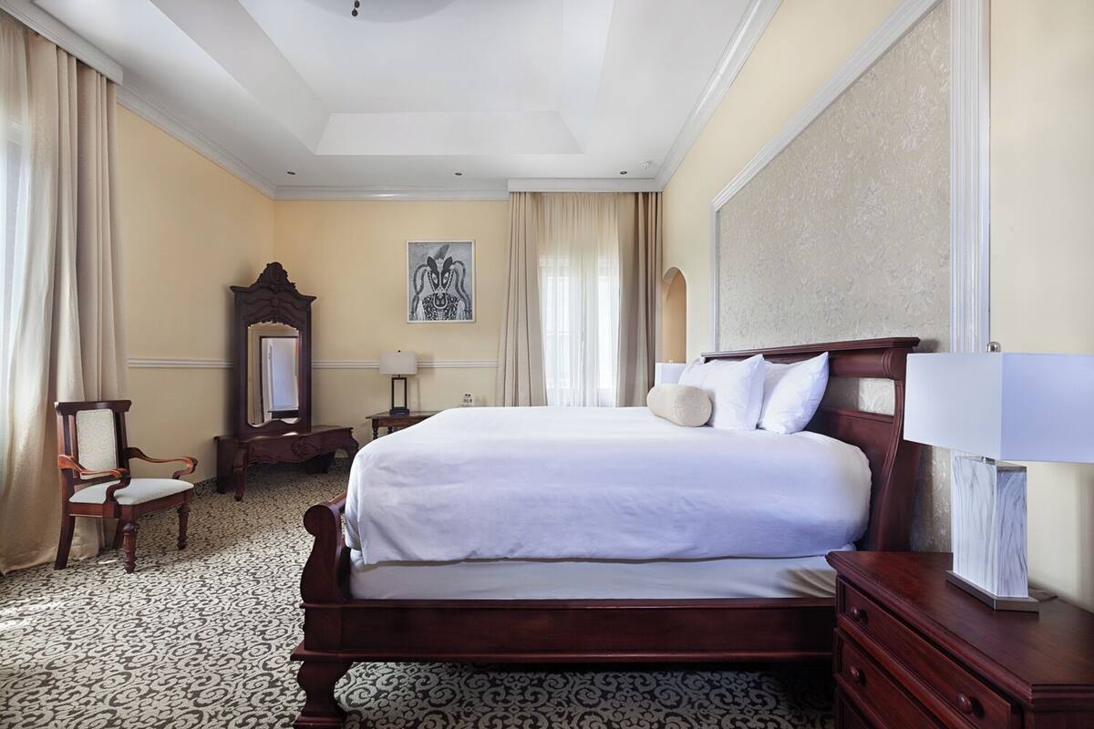 A hotel room with a large bed, a wooden dresser, a chair, a desk, and a mirror.