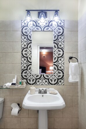 A bathroom with a white sink, a mirror, and patterned tiles. - Hotel La Perla León (León)