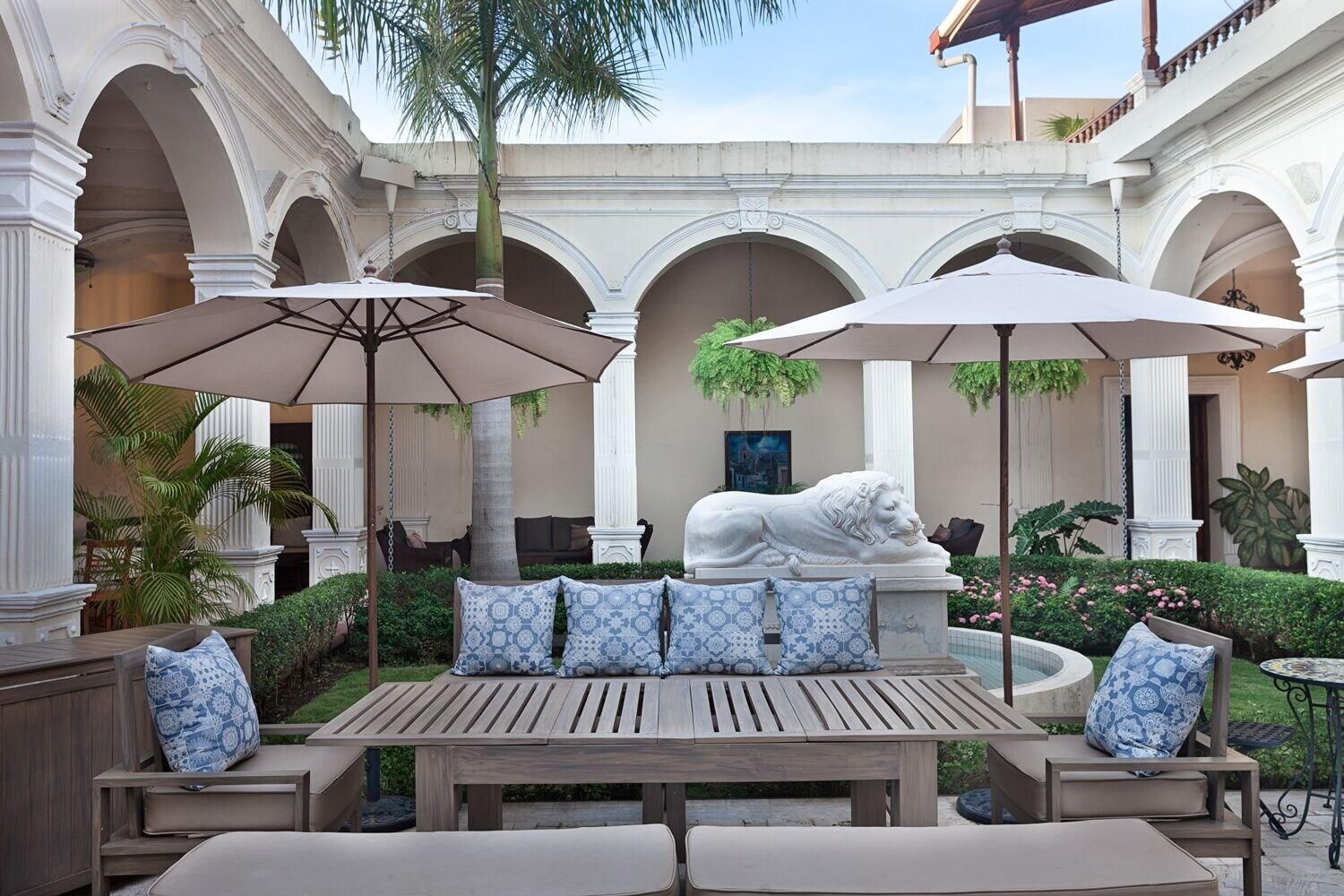 A courtyard with a wooden bench, two umbrellas, and a lion statue.