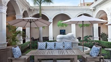 A courtyard with a wooden bench, two umbrellas, and a lion statue.