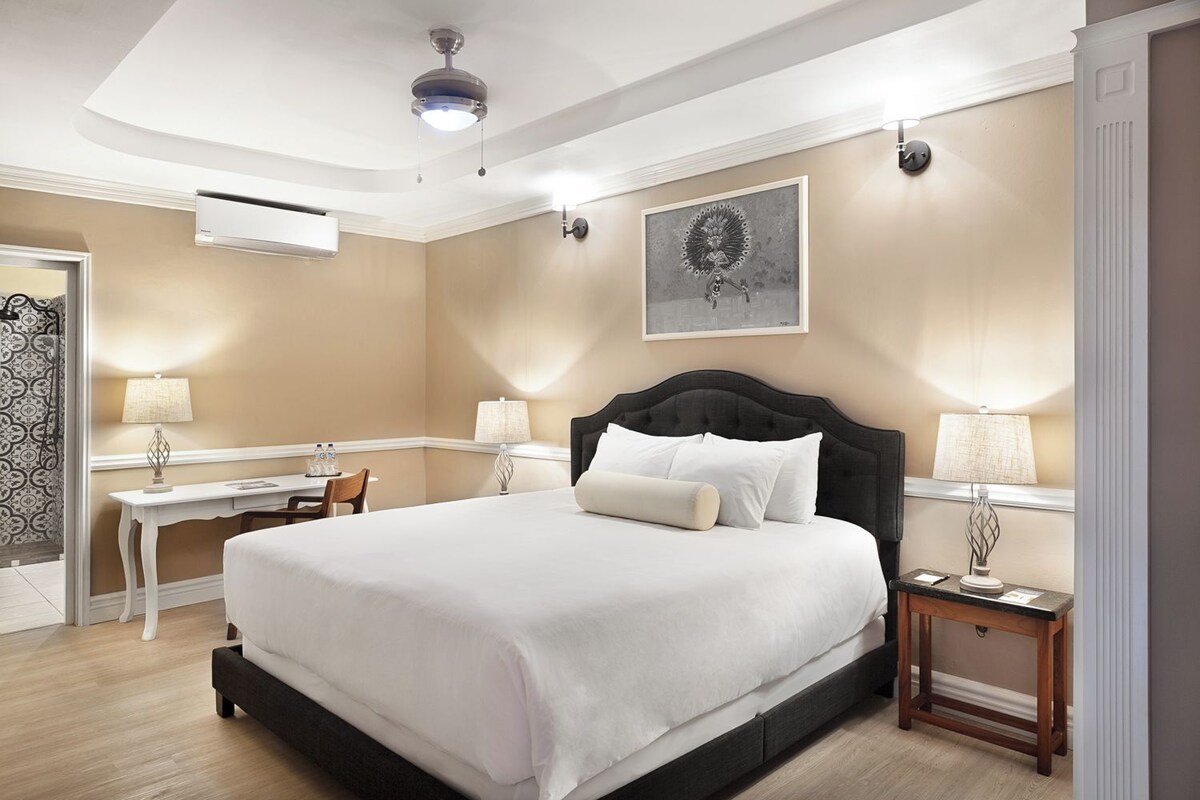 A hotel room with a large bed, bedside tables, a desk, and a ceiling fan.