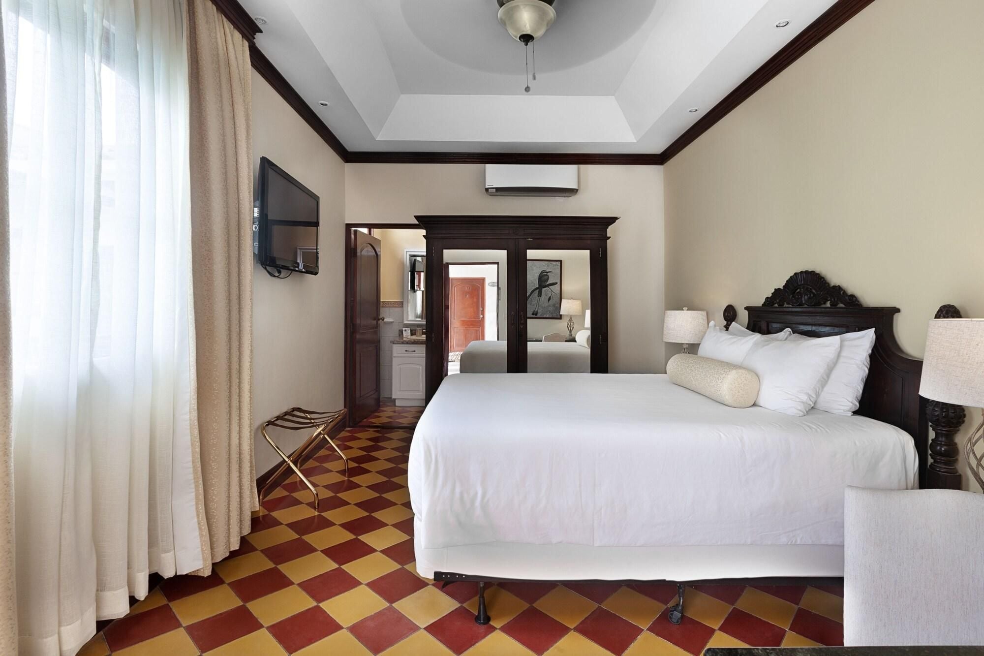 Habitación de hotel con cama, televisor, espejo, puerta y mostrador de recepción.