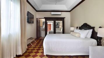 Habitación de hotel con cama, televisor, espejo, puerta y mostrador de recepción.