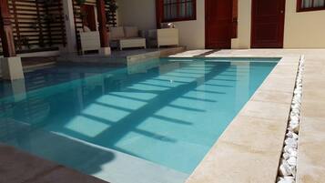 A swimming pool with a tiled deck, wooden pergola, and outdoor furniture.