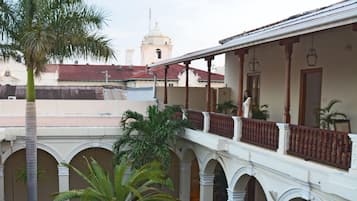 A courtyard with a palm tree, a building with arches, and a tower in the background.