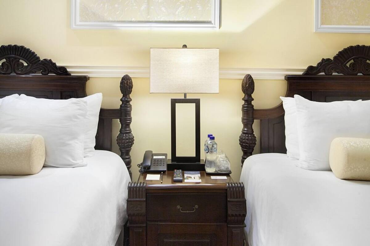 A hotel room with two beds, a nightstand, a lamp, and a mirror.