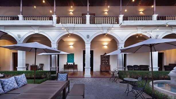 An outdoor patio with wooden furniture, umbrellas, and a pool. - Hotel La Perla León (León)