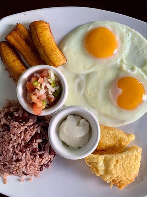 A plate with fried eggs, plantains, rice, and a small bowl of salsa. - Hotel La Perla León (León)