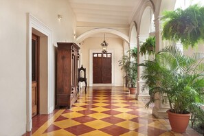 A hallway with a checkered floor, a wooden door, and potted plants. - Hotel La Perla León (León)