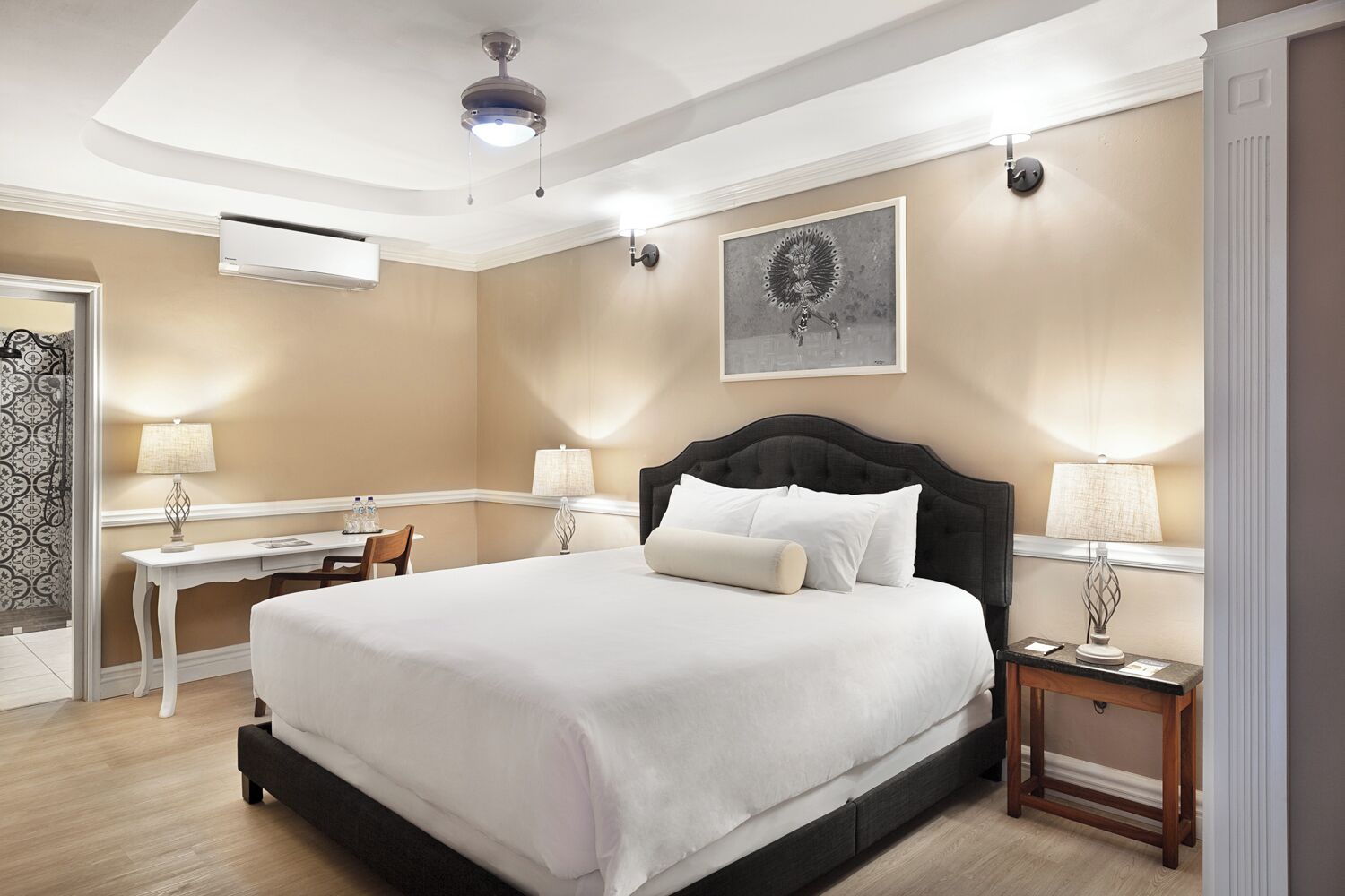 Habitación de hotel con cama, escritorio, silla, ventilador de techo y lámpara de pared.