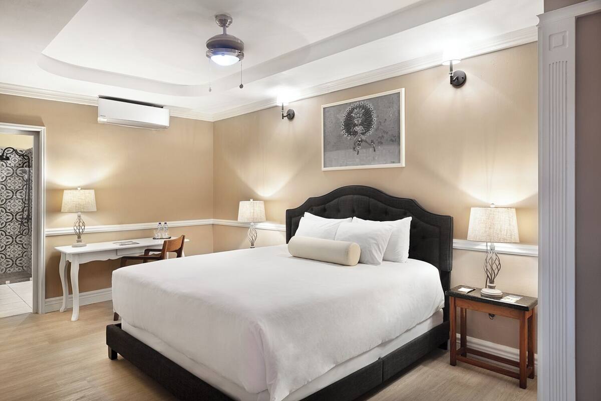 A hotel room with a large bed, bedside tables, a desk, and a ceiling fan.