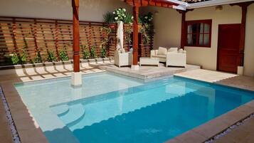 Una piscina con una pérgola, asientos al aire libre y una valla de madera.