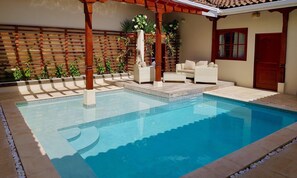 Una piscina con una pérgola, asientos al aire libre y una valla de madera.