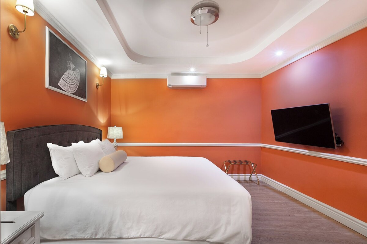 Una habitación de hotel con una cama grande, un televisor de pantalla plana montado en la pared y un equipo de aire acondicionado.