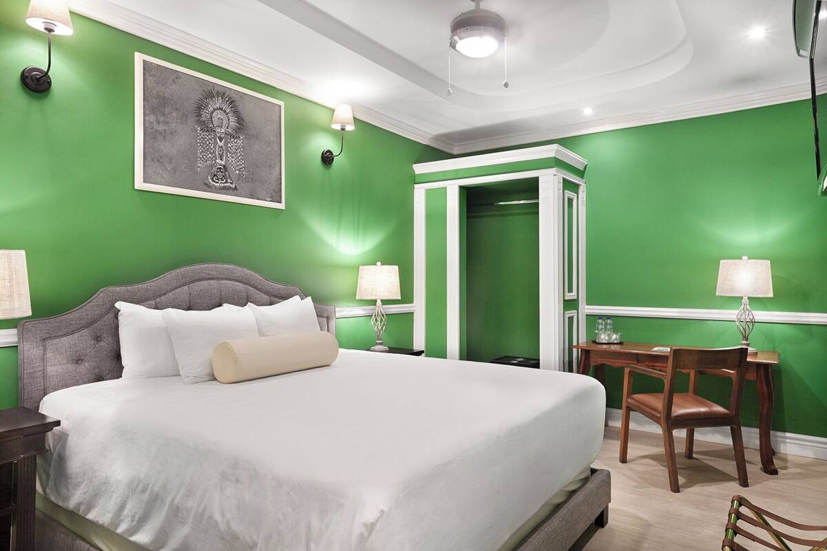 A hotel room with a large bed, a desk with a chair, and a green accent wall.