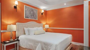 Un dormitorio con pared naranja, cama blanca, dos lámparas de noche y un ventilador de techo.
