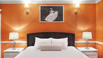 A bedroom with an orange wall, a large bed with white bedding, two bedside tables with lamps, and a framed artwork above the bed.