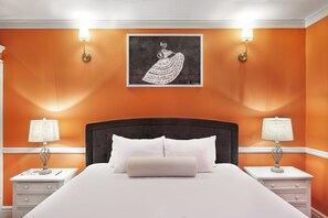A bedroom with an orange wall, a large bed with white bedding, two bedside tables with lamps, and a framed artwork above the bed. - Hotel La Perla León (León)