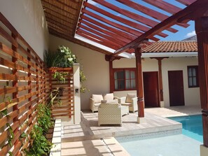 A covered outdoor area with a pool, wicker furniture, and a wooden fence with climbing plants. - Hotel La Perla León (León)