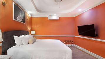A hotel room with a large bed, a flat-screen TV, an air conditioning unit, and a framed picture on the wall.
