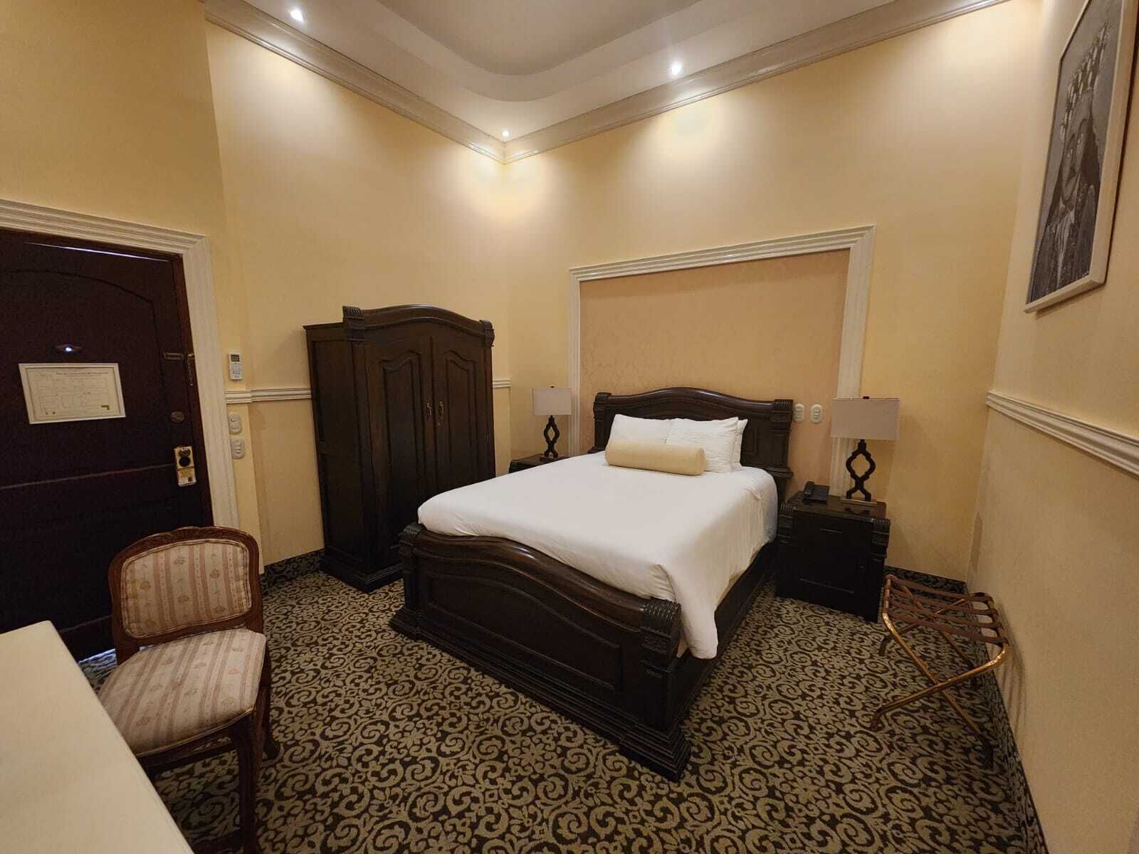 Una habitación de hotel con una cama grande, un armario, un escritorio y una silla.