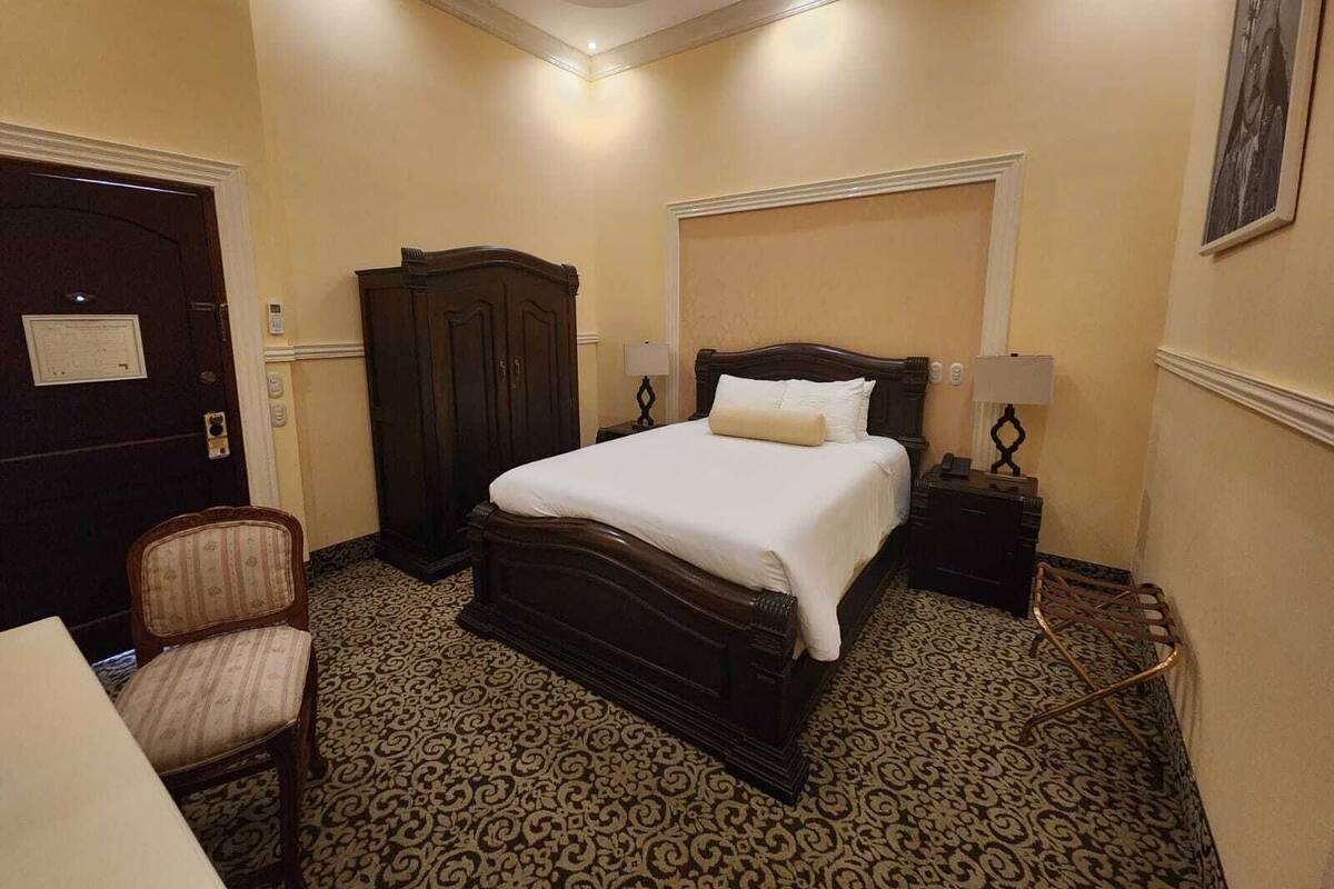 A hotel room with a large bed, a wardrobe, a desk, and a chair.