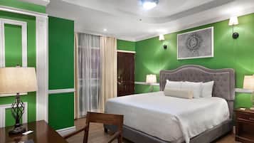 A bedroom with a large bed, a desk, a chair, a ceiling light, and a door.