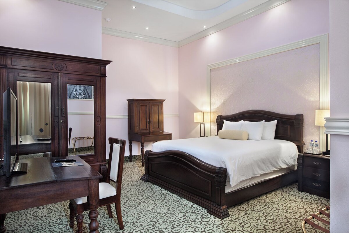 A hotel room with a large bed, a desk, a chair, and a wardrobe.