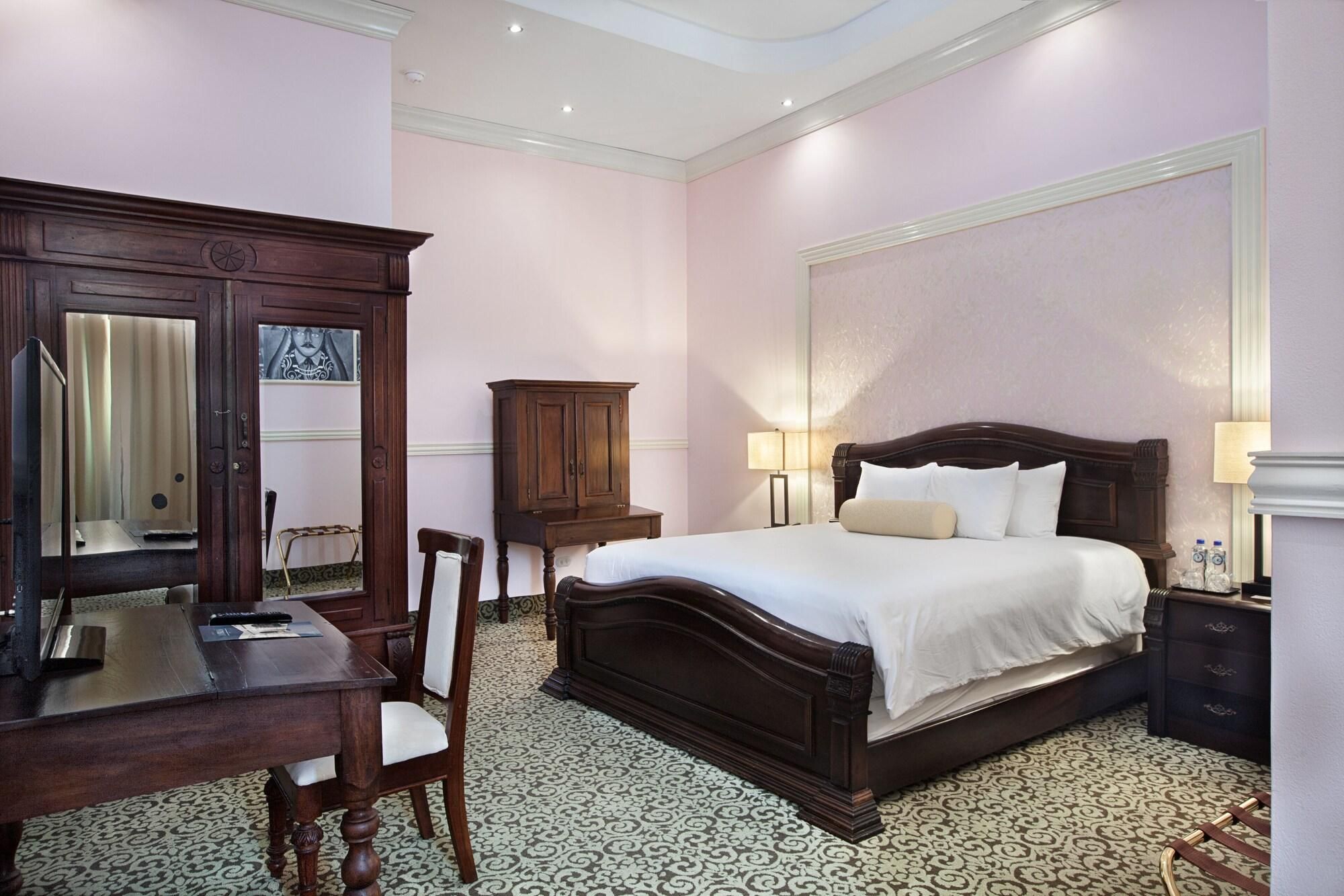 A bedroom with a bed, a desk, a chair, a cabinet, and a mirror.