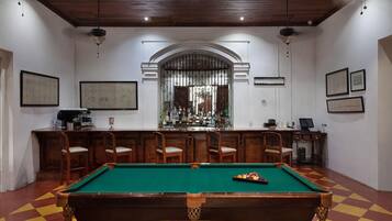 Una sala de billar con mesa de pool, zona de bar y sillas.