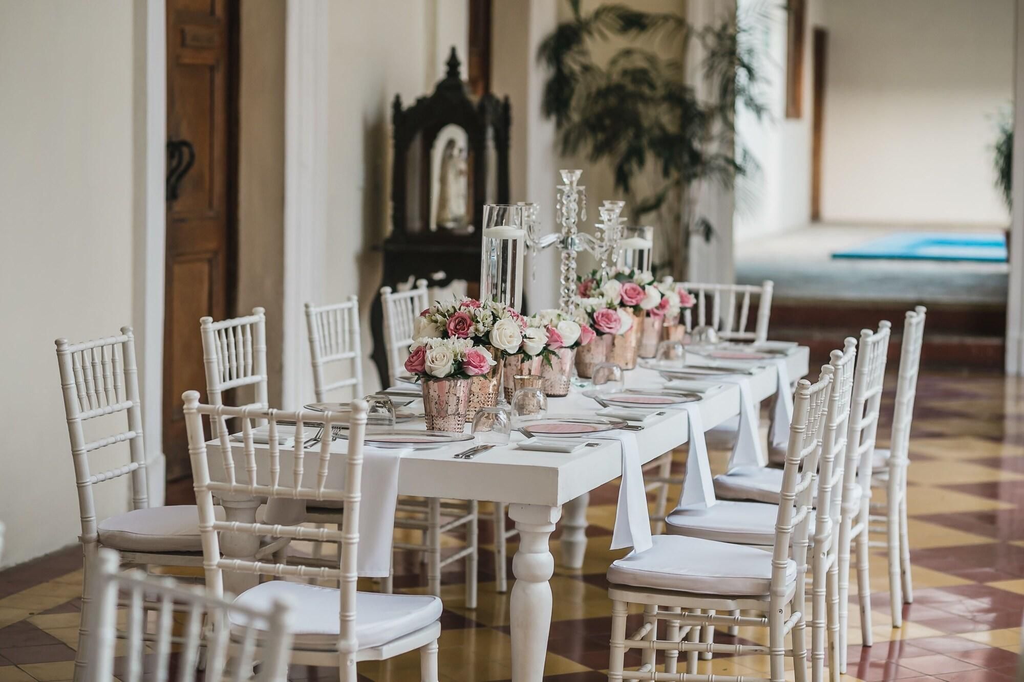 A long dining table with white chairs, floral centerpieces, and a chandelier.