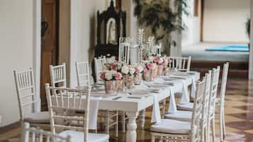 A long dining table with white chairs, floral centerpieces, and a chandelier.