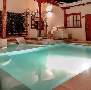A swimming pool with lounge chairs, a pergola, and a door with a window.