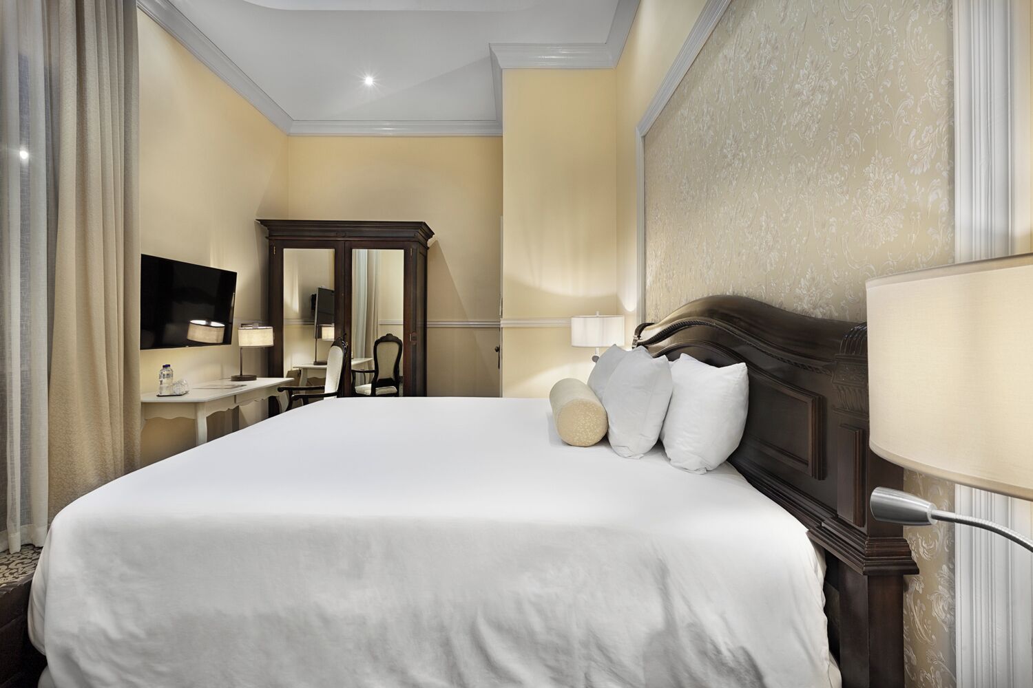 Habitación de hotel con una cama grande, un escritorio con silla, un televisor y un espejo.