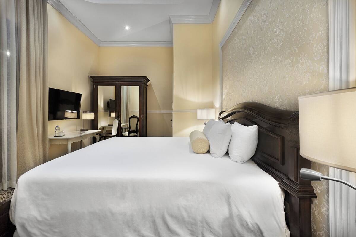 A hotel room with a large bed, a desk with a chair, a television, and a mirror.