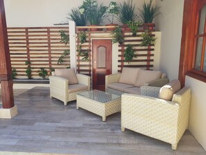 Eine Terrasse mit Korbmöbeln, einem Glastisch und einer Holztür.
