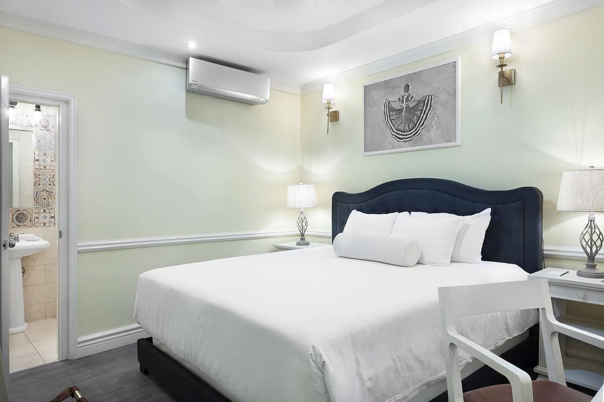 Habitación de hotel con una cama, una silla, una mesita de noche, aire acondicionado de pared y un adorno mural.