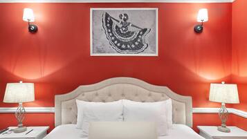 A hotel room with a red wall, a large bed with white bedding, two bedside tables with lamps, and a framed artwork above the bed.